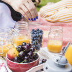 woman-s-hand-eating-blueberry-with-mango-juice-jar-fruits